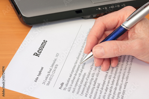 Hand with Pen Proofreading a Resume by Laptop