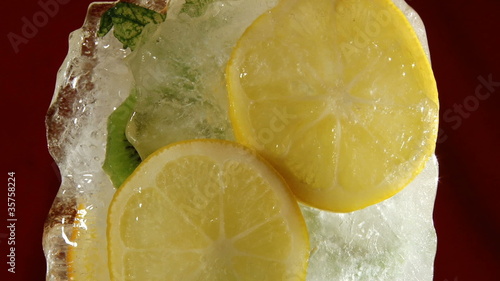 Frozen fruits in ice (kiwi, orange and lemon) - red background