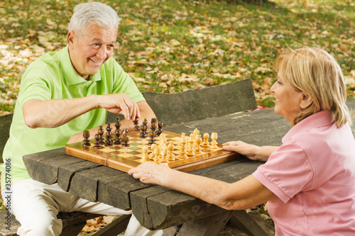 happy senior couple playing chess on a park bench photo