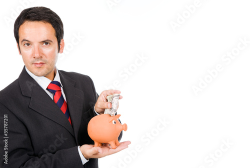 Business man inserting money into a piggy moneybox, isolated on