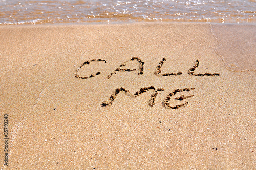Call me text written on the beach sand