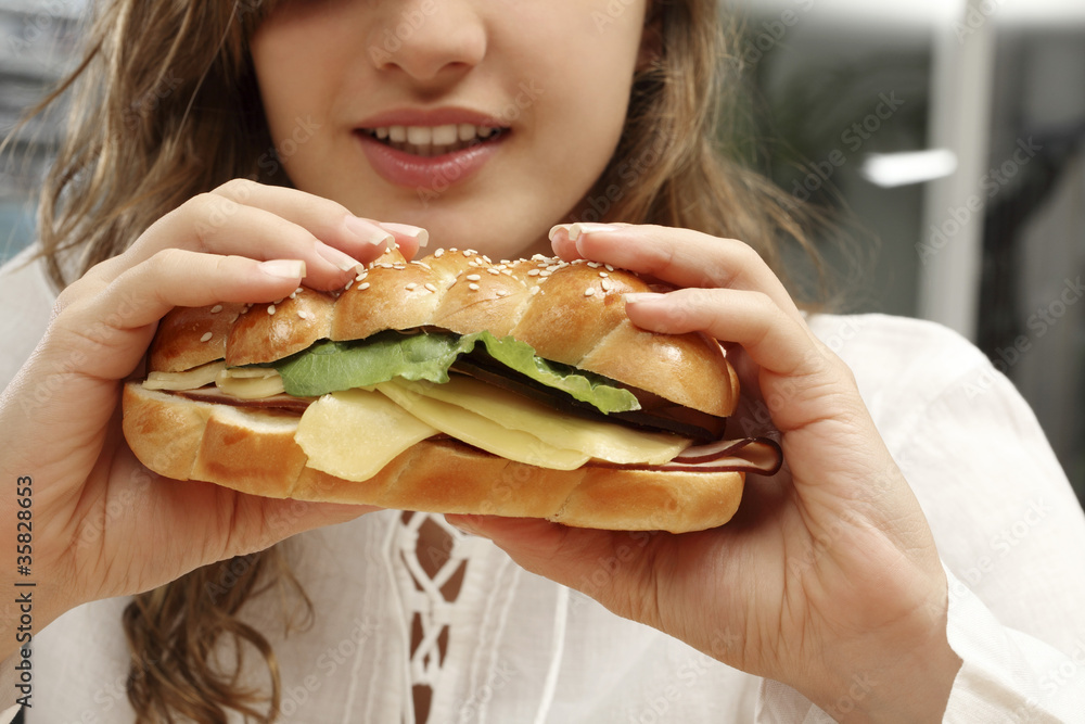 Femme mangeant un sandwich viennois au jambon de dinde, fromage et légumes Femme mangeant un sandwich viennois au jambon de dinde, fromage et légumes