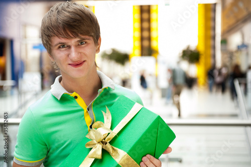Wall Mural Portrait of young man inside shopping mall with gift box sitting