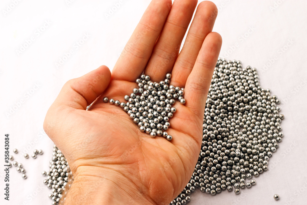 BB pellets in hand over pile of silver pellets