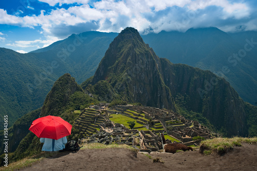 Tourist under the shade of a red umbrella looking at Machu Picch