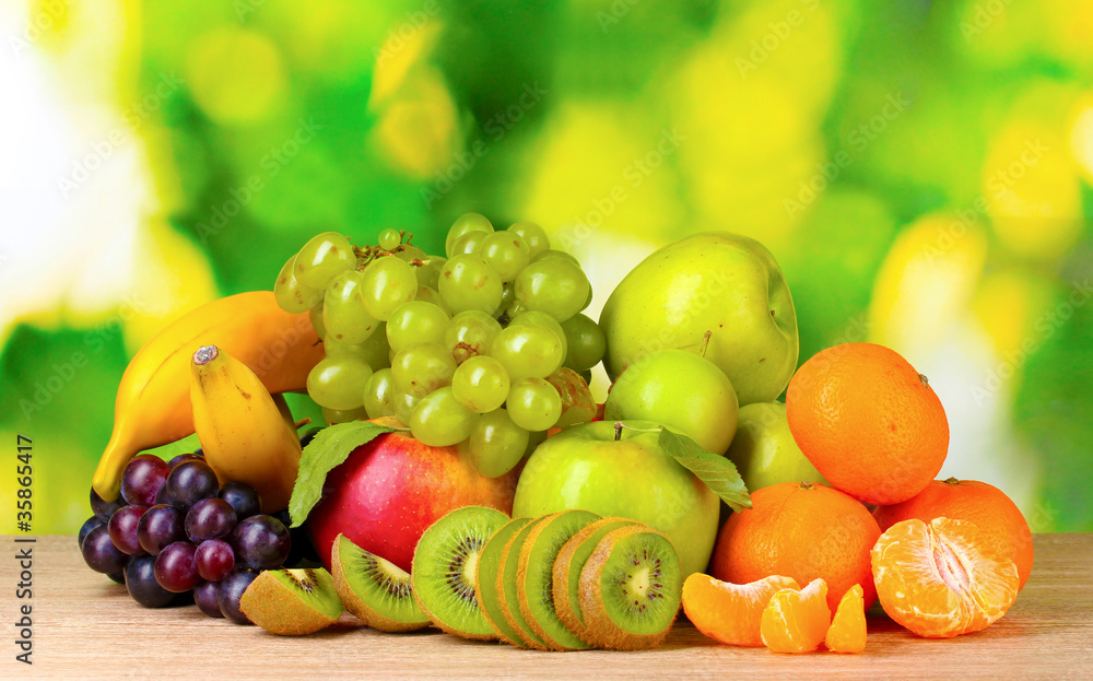 Ripe juicy fruits on wooden table on green background