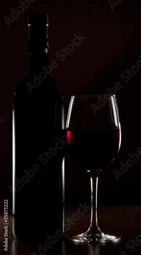 Backlit detail of a glass of red wine and the bottle