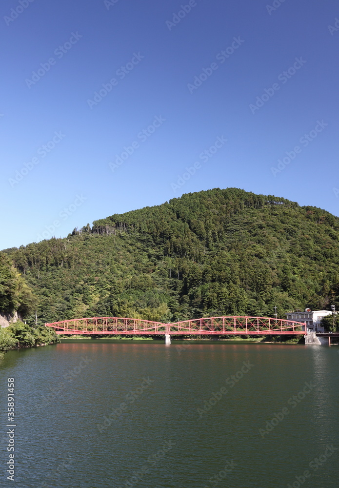 ダム湖にかかるピンク色の鉄橋と山と空と水面