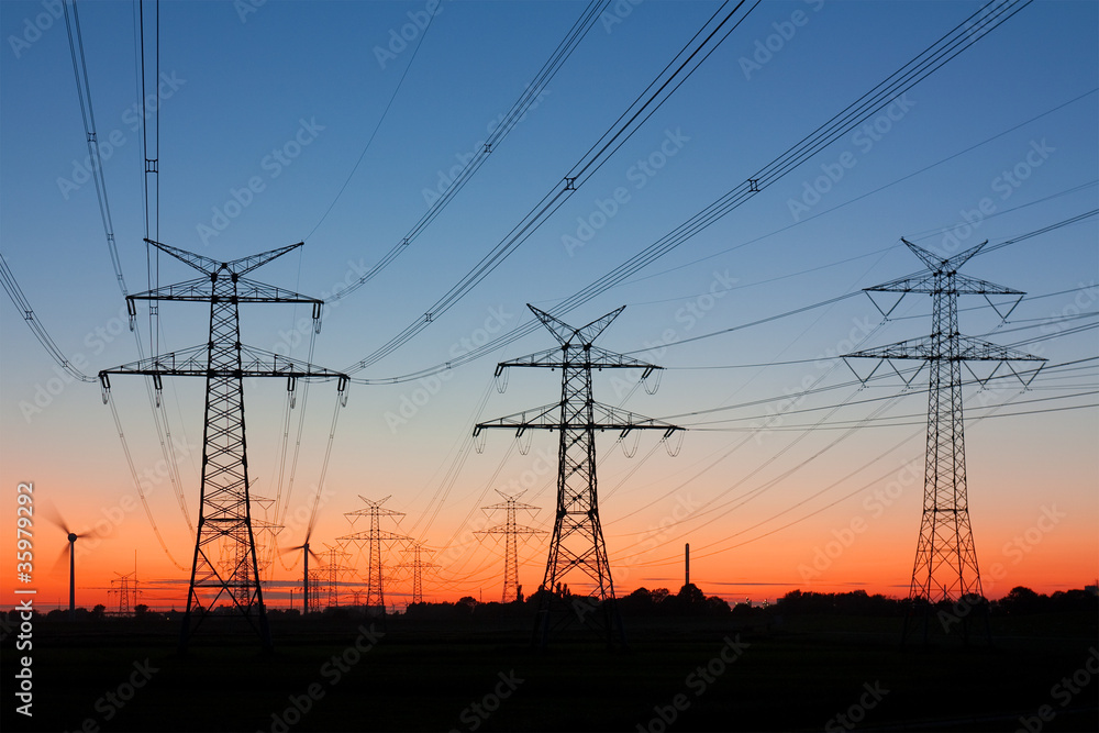 Strommasten bei Sonnenuntergang, am Horizont Windräder