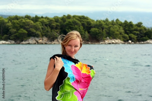 Young smiling woman shelters herself behind pareo near sea water