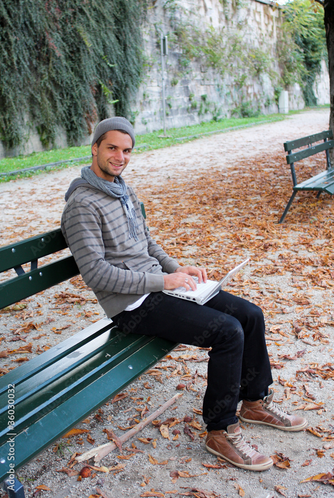 Fototapeta premium Man writing on Netbook on a Bench Outdoors