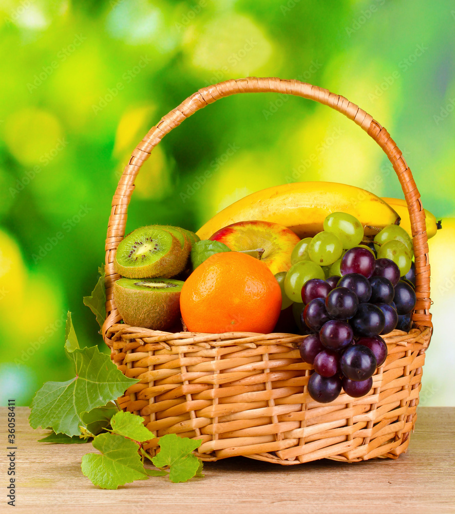 Ripe juicy fruits in basket on wooden table on green background