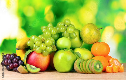 Ripe juicy fruits on wooden table on green background