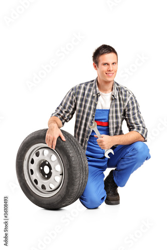 A male mechanic posing with a spare tire and holding a wrench