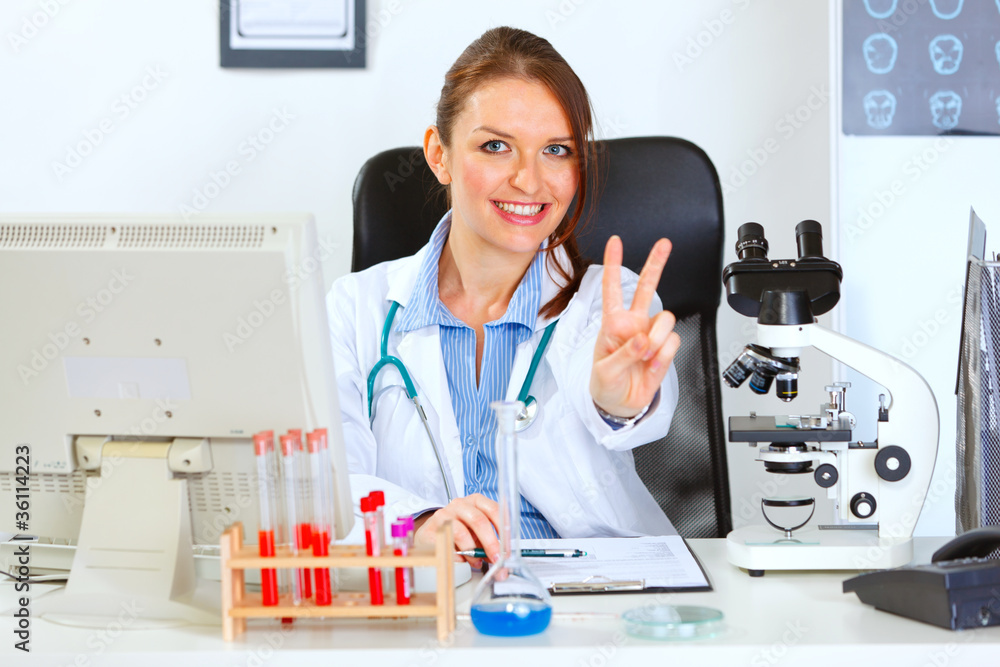 Female medical doctor sitting at table and showing victory