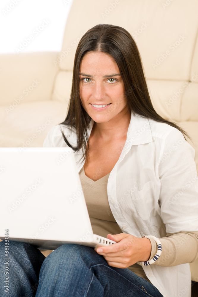 Woman with laptop sitting by couch smiling Woman with laptop sitting by couch smiling