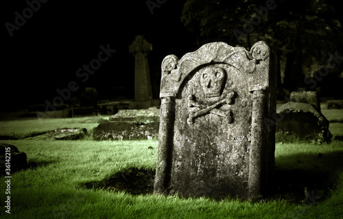Fotografija Gravestone with skull and bones in old cemetery, dramatic light