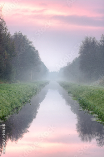 A long, straight canal, disappearing in the morning haze