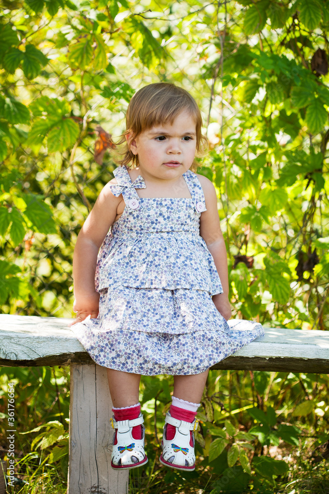 Little girl sitting on a bench in the garden Little girl sitting on a bench in the garden