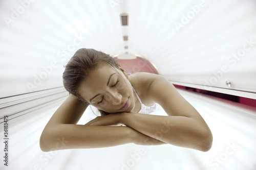 Beautiful young woman tanning in solarium photo