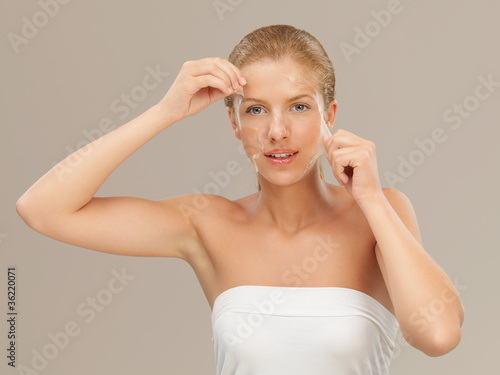 young woman peeling off a facial mask smiling photo