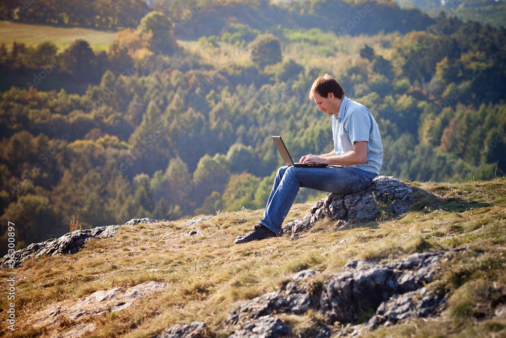 young man using laptop sitting on the grass on the hillside young man using laptop sitting on the grass on the hillside