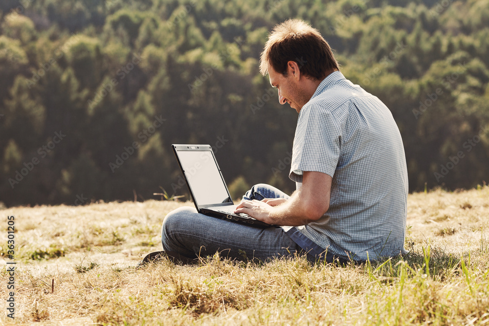 young man using laptop sitting on the grass on the hillside young man using laptop sitting on the grass on the hillside