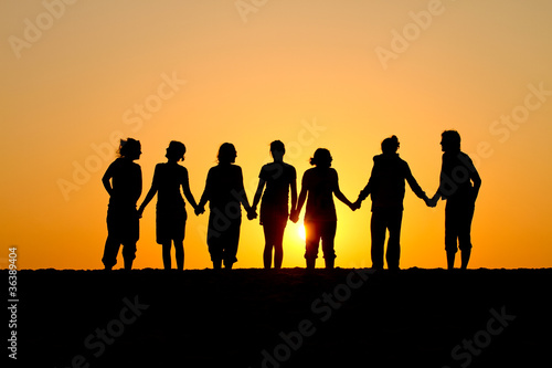 silhouette of group of friends standing in sunset at beach