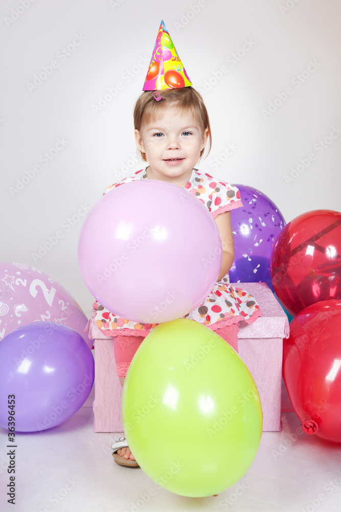 Obraz premium Little girl with balloons sitting on the gift in studio
