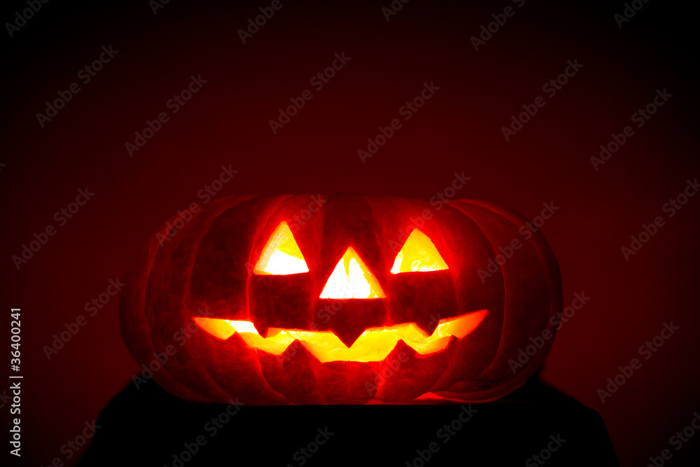 Fototapeta premium Orange scarry pumpkin with burning eyes, nose and mouth on dark