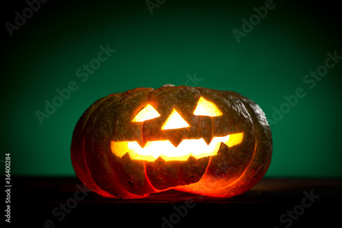 Orange scarry pumpkin with burning eyes, nose and mouth on green