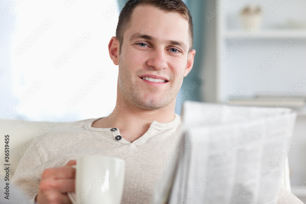 Smiling man having a tea while reading the news Smiling man having a tea while reading the news