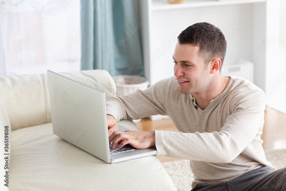Smiling man sitting on a carpet while using a notebook Smiling man sitting on a carpet while using a notebook
