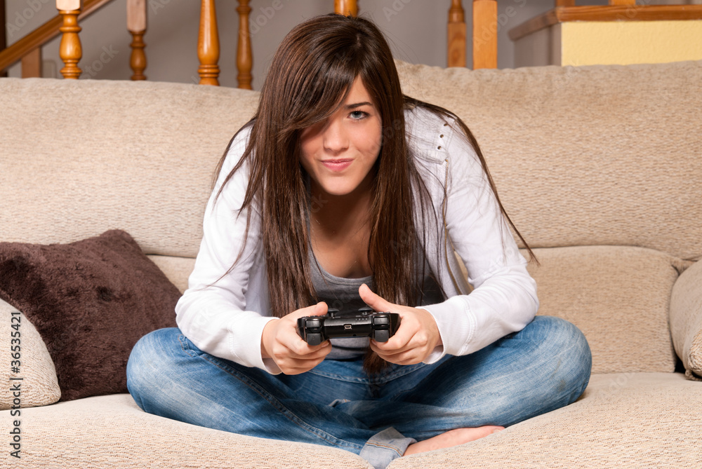 Obraz premium Young female playing video-games concentrating on sofa at home