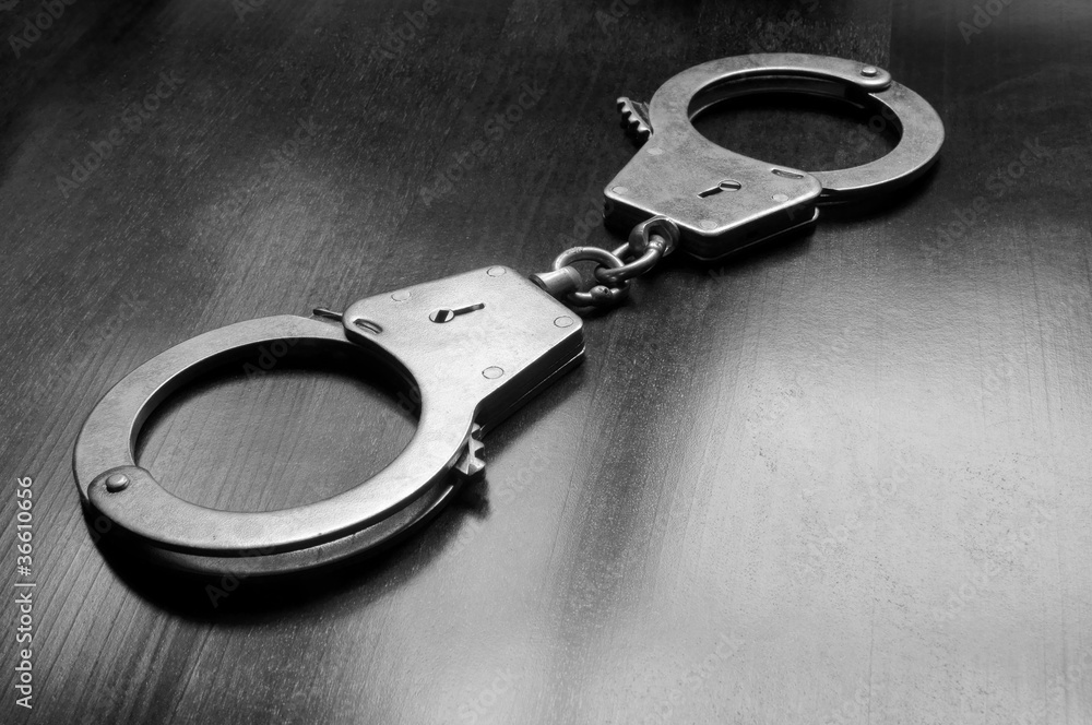 Steel metallic handcuffs on wooden table Steel metallic handcuffs on wooden table