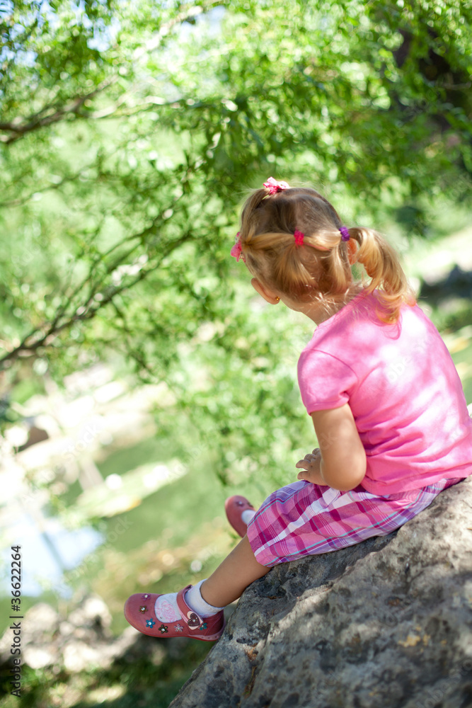 Naklejka premium Little girl sitting in the park, backview