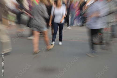 Motion and zoom blurry people walking on city street