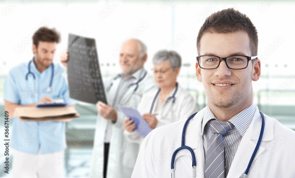 Portrait of young doctor with team in background Portrait of young doctor with team in background
