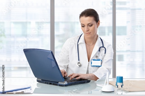 Female doctor sitting at table with laptop