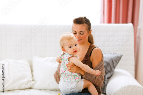 Funny baby sitting on mamas knees and looking back