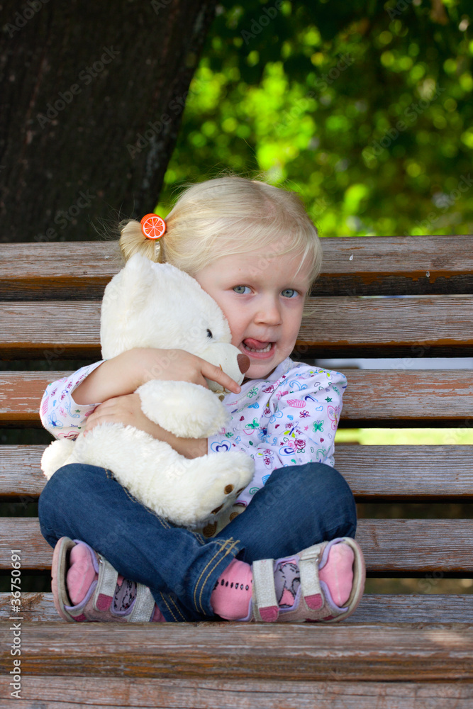 girl sitting  on a bench with toy bear at the park.