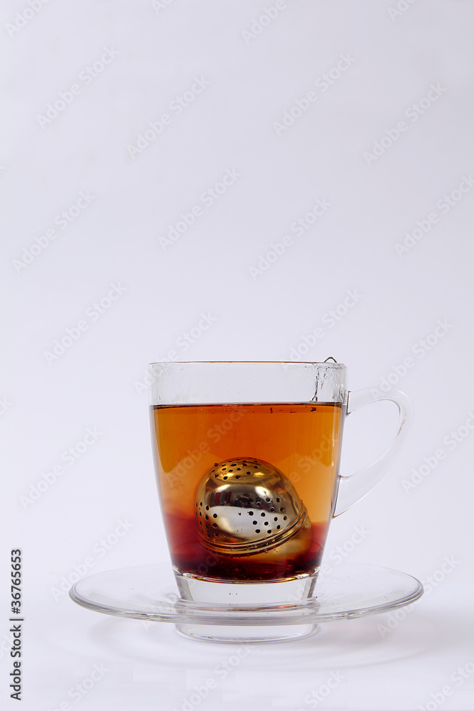 Tee-Ei in Tasse aus Glas auf weißem Untergrund Tee-Ei in Tasse aus Glas auf weißem Untergrund