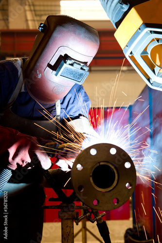 factory worker welding metal and sparks spreading