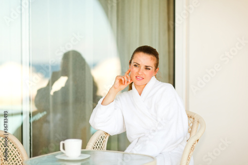 Thoughtful pretty woman in bathrobe sitting at table on terrace © Alliance