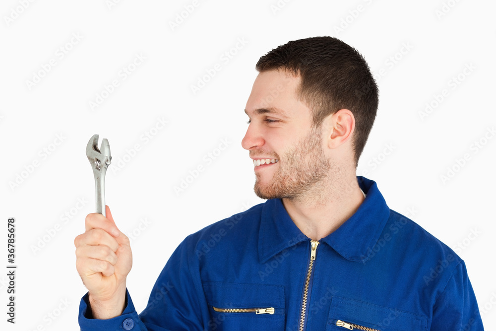 Smiling young mechanic in boiler suit looking at his wrench Smiling young mechanic in boiler suit looking at his wrench