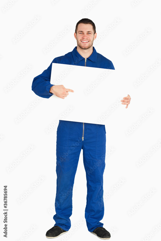 Smiling young mechanic in boiler suit pointing on banner in his Smiling young mechanic in boiler suit pointing on banner in his
