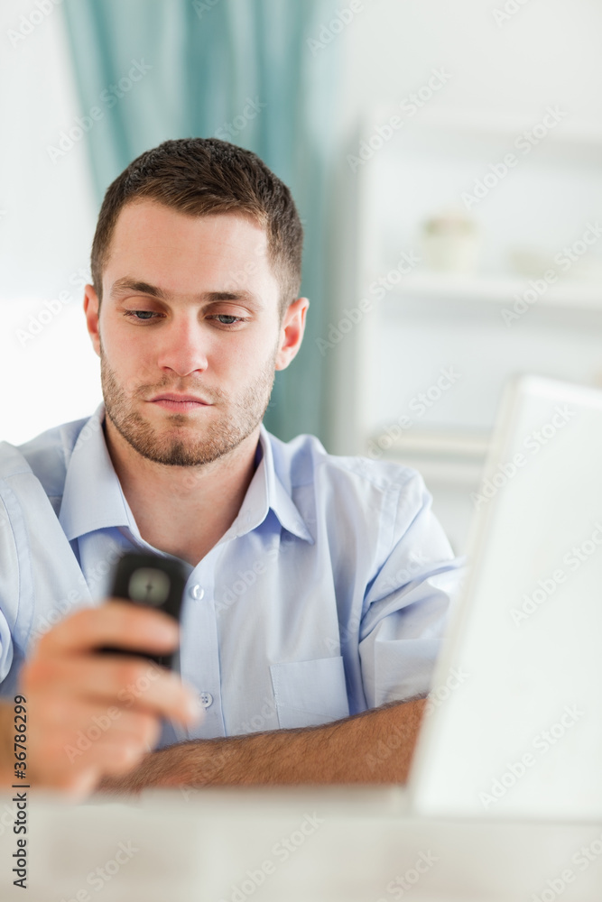 Fototapeta premium Businessman texting on his cellphone sitting behind his desk