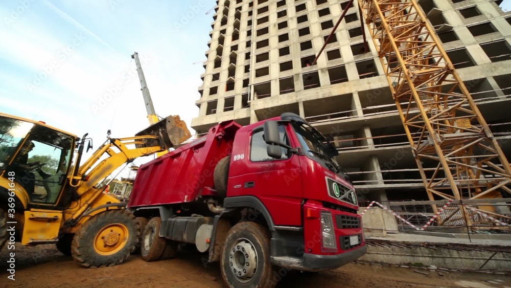 Excavator loads truck at construction site of living house