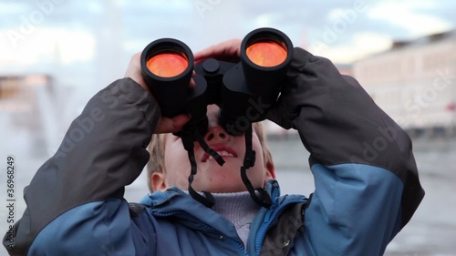 Boy stand on waterfront, looking through binoculars
