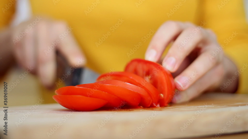 Woman is cutting a tomato into slices, close up